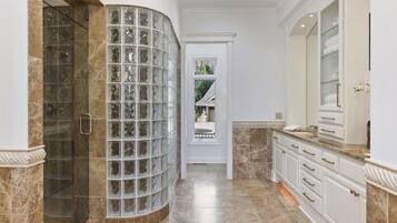 A bathroom with a glass block shower enclosure, marble flooring, and white cabinetry.