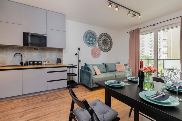 A modern living room with a cozy sofa, a wall-mounted TV, and a dining area adjacent to the kitchen.