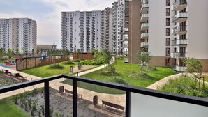 A residential building with multiple floors, balconies, and a well-maintained garden area with pathways and benches.