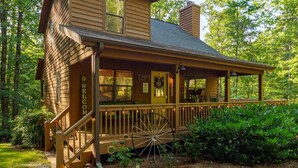 A wooden cabin with a porch, a large wheel, and a 'WELCOME' sign.