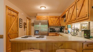 A kitchen with wooden cabinets, a stainless steel refrigerator, a microwave, and a stove. There are two wooden stools at the kitchen island.
