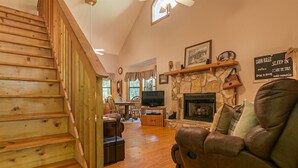 A wooden staircase leading to a living room with a stone fireplace, a television, and a couch.