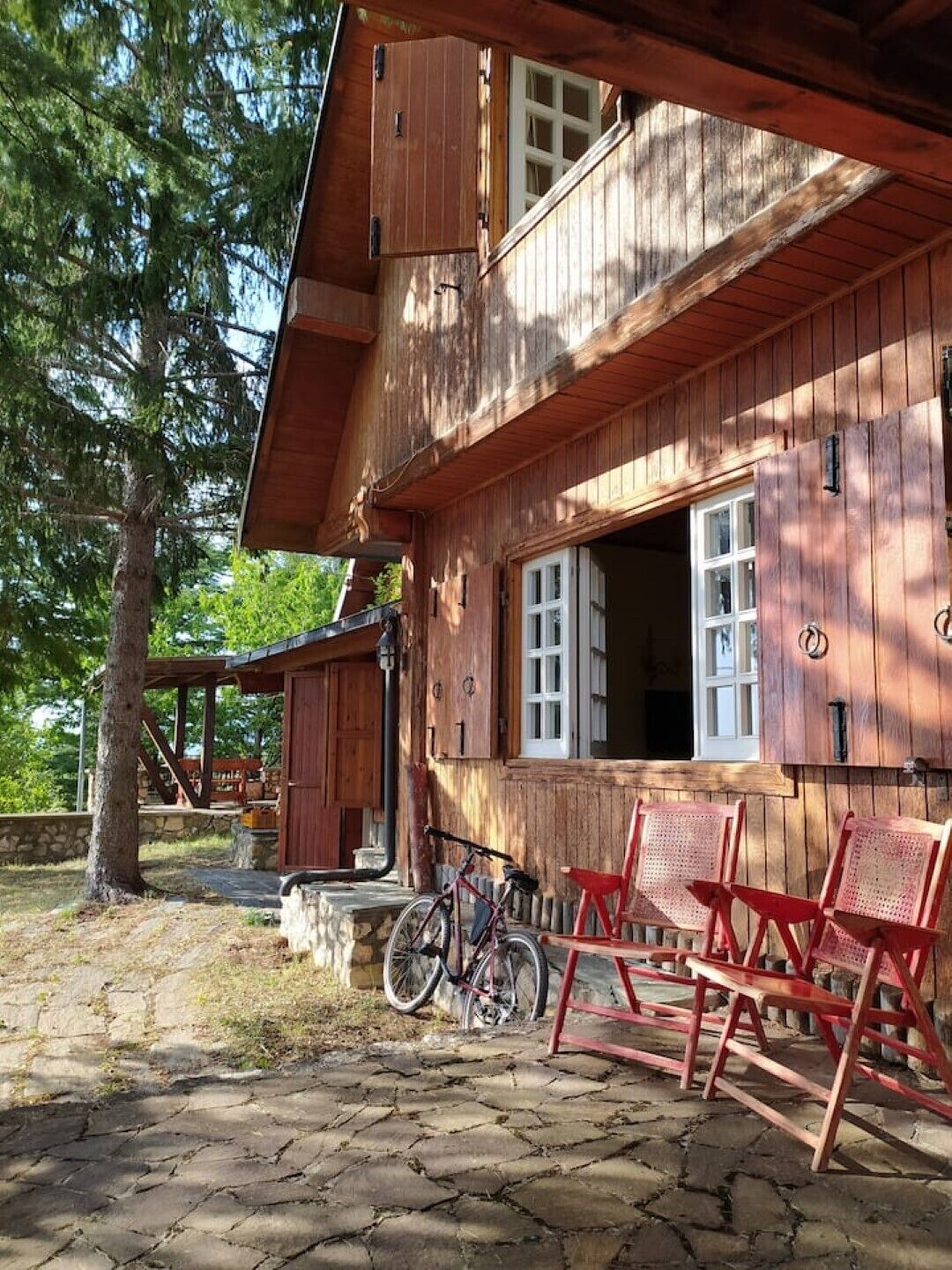 A wooden cabin with a porch, a bicycle, and red chairs.