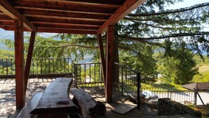 Un pavillon en bois, doté d’une table et de bancs, entouré d’une rambarde en métal, et offrant une vue sur un paysage montagneux.