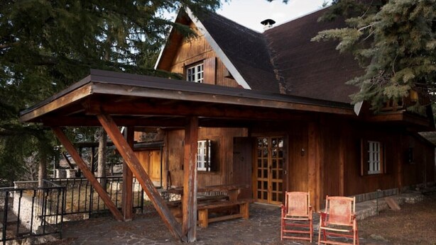 Une cabane en bois avec une véranda, un banc et deux chaises.