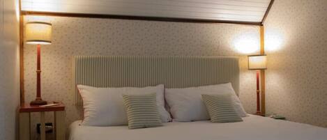 A neatly made bed with a striped headboard, two bedside lamps, and a window with blinds.