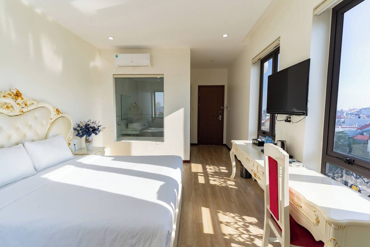 A hotel room with a large bed, a desk with a chair, a TV mounted on the wall, and a window with a city view.