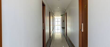 A long, narrow hallway with a patterned border at the floor, doors on both sides, and a ceiling light.