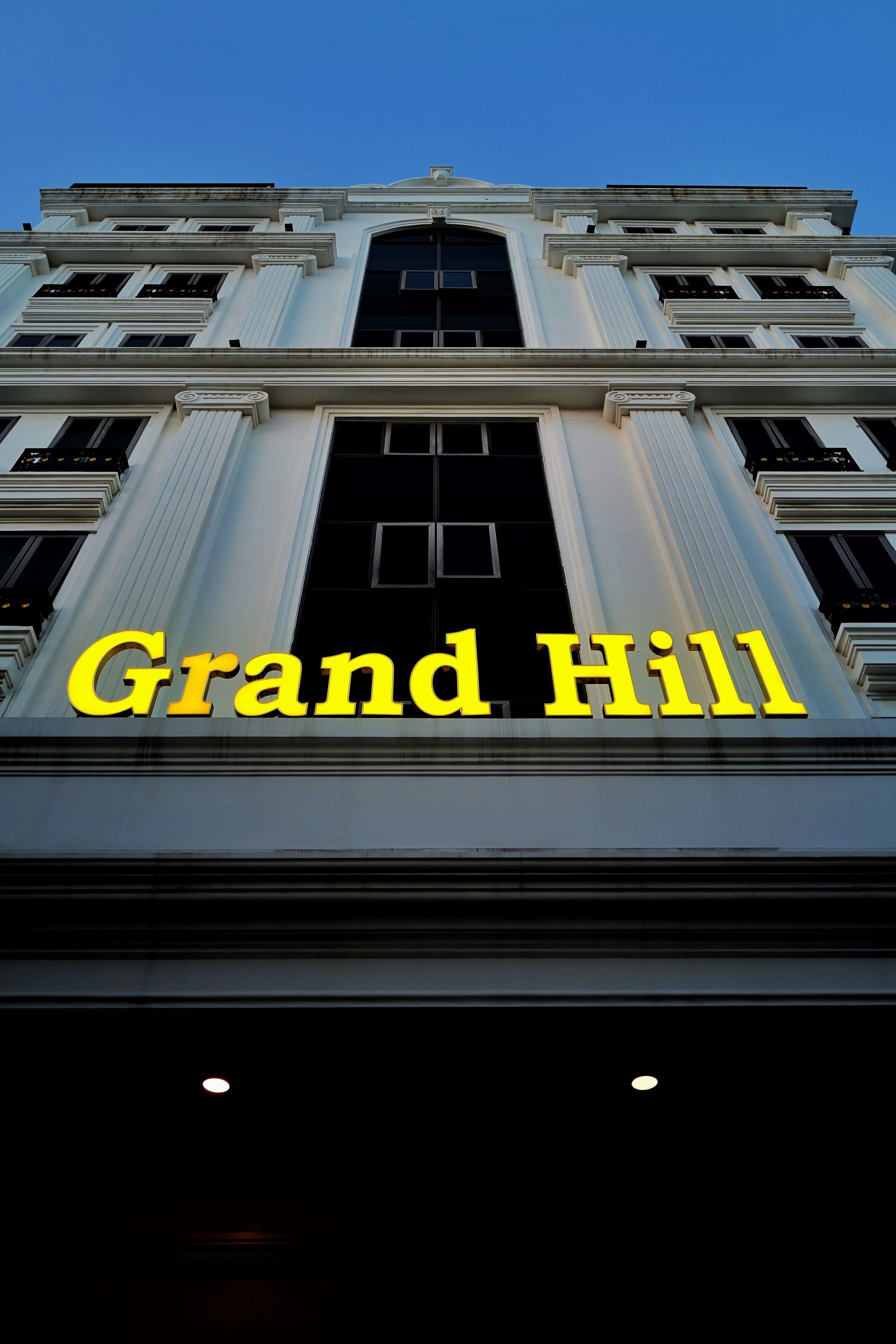 A building with the sign "Grand Hill" illuminated in yellow.