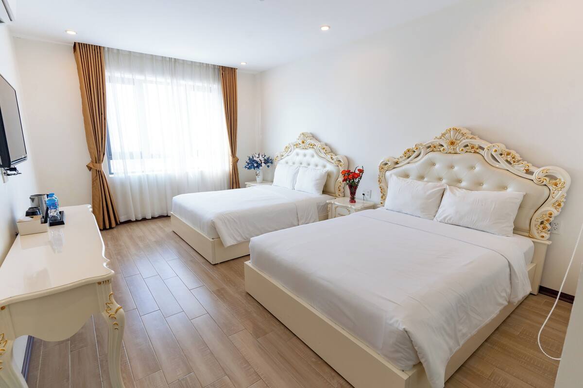 A hotel room with two beds, a desk, a TV, and a window with curtains.