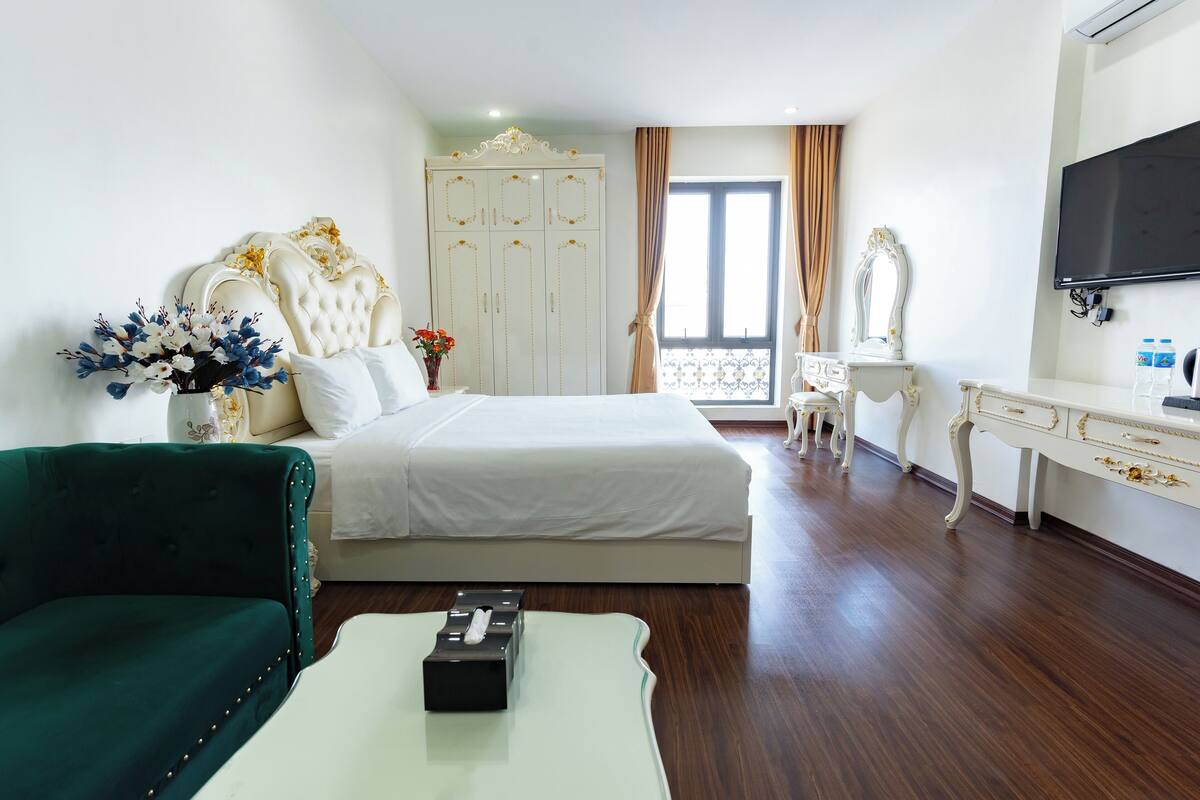 A hotel room with a large bed, a green sofa, a white dresser, and a TV.