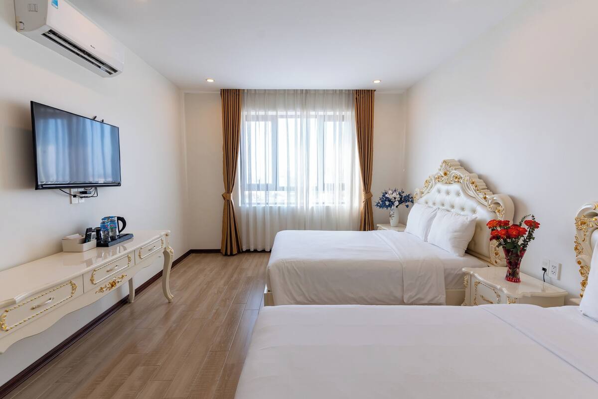 A hotel room with two beds, a TV, a dresser, and a window with curtains.