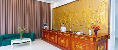A reception area with a wooden reception desk, a green sofa, and a large golden mural on the wall.