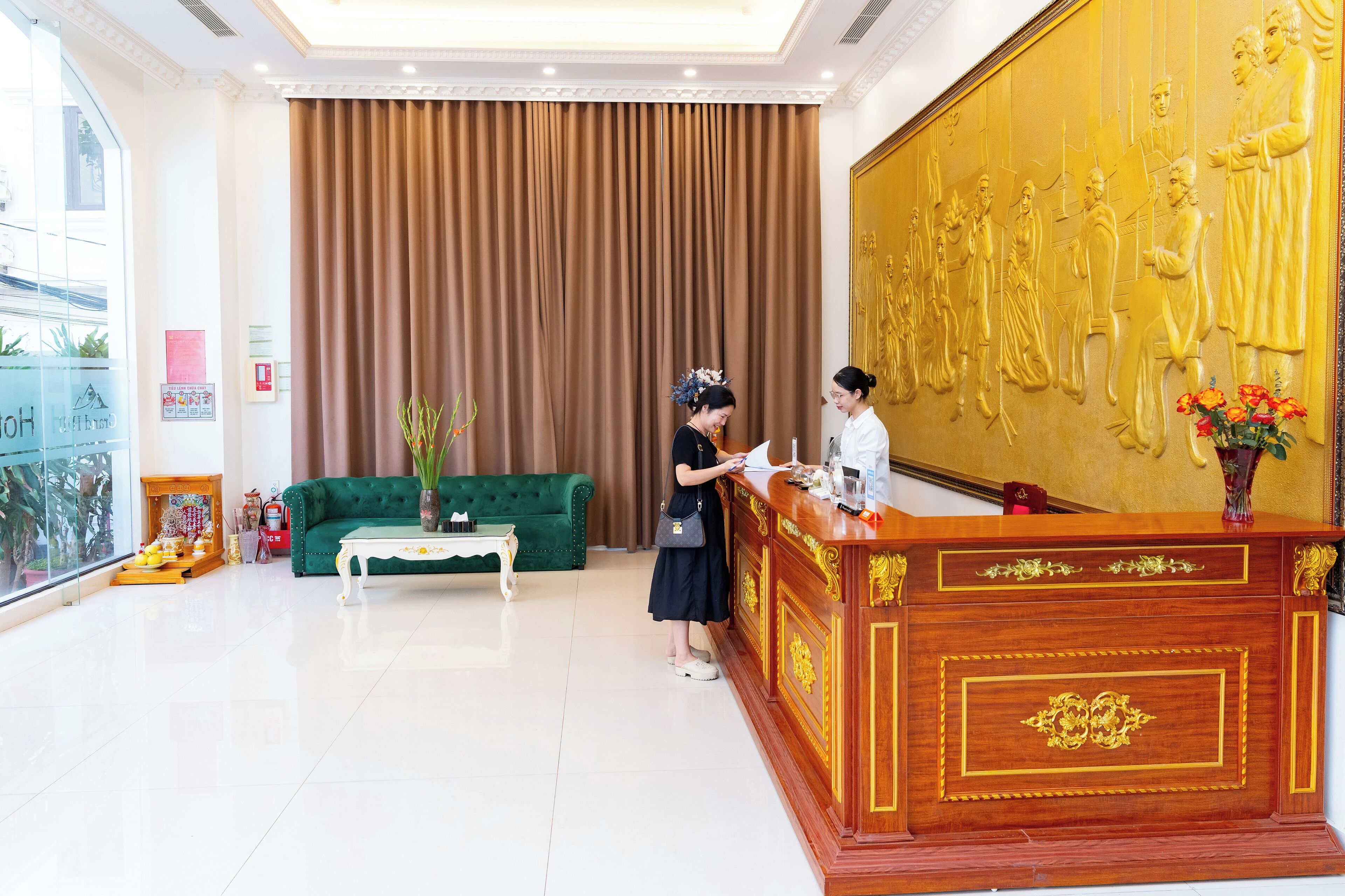 Ein Empfangsbereich mit einem grünen Sofa, einem hölzernen Empfangsschalter und einer großen, goldenen Statue an der Wand.