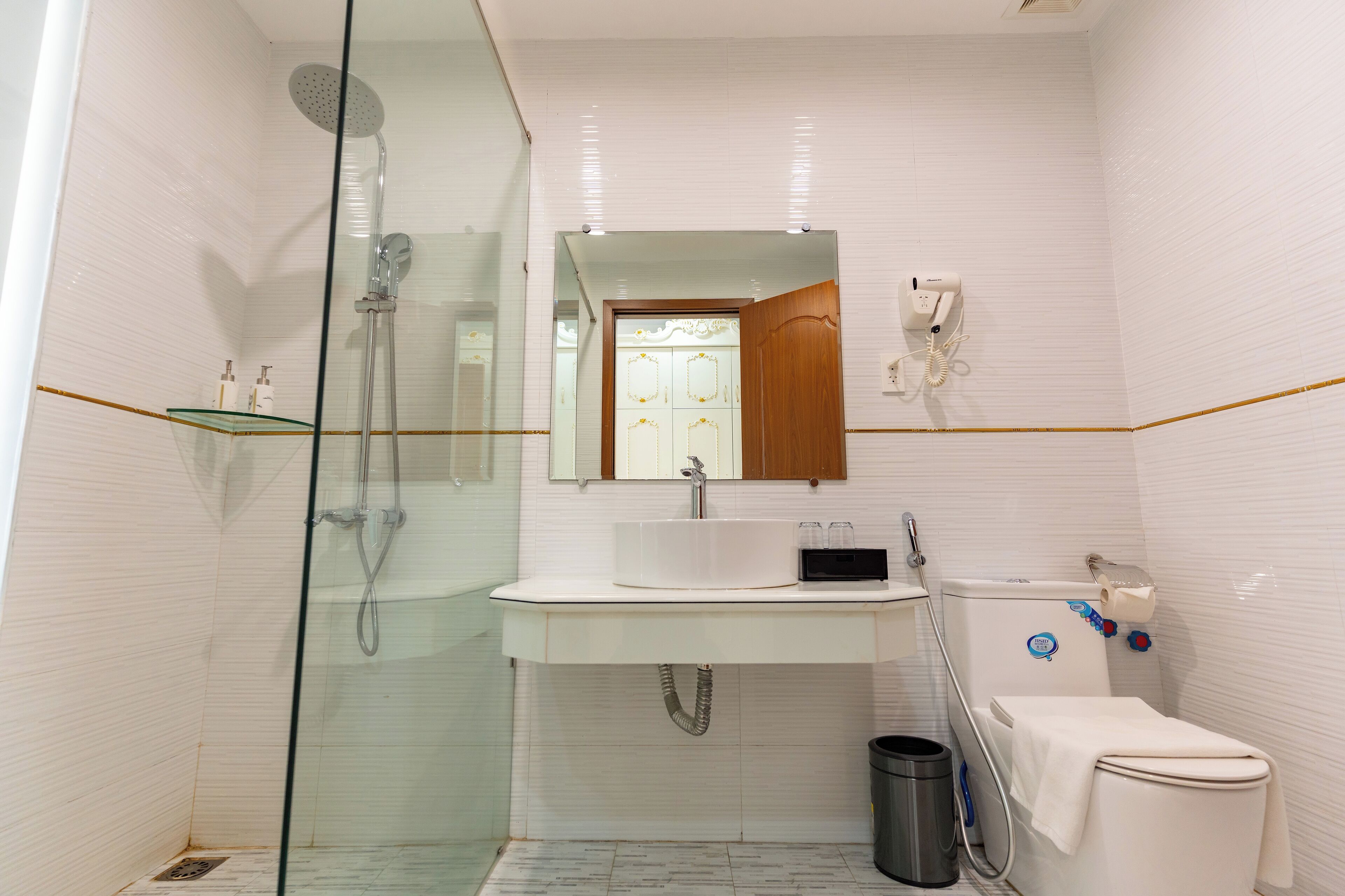 Un baño moderno con ducha de vidrio, un lavamanos blanco con espejo y un inodoro con dispensador de toallas de papel.