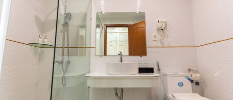 Un baño moderno con ducha de vidrio, un lavamanos blanco con espejo y un inodoro con dispensador de toallas de papel.