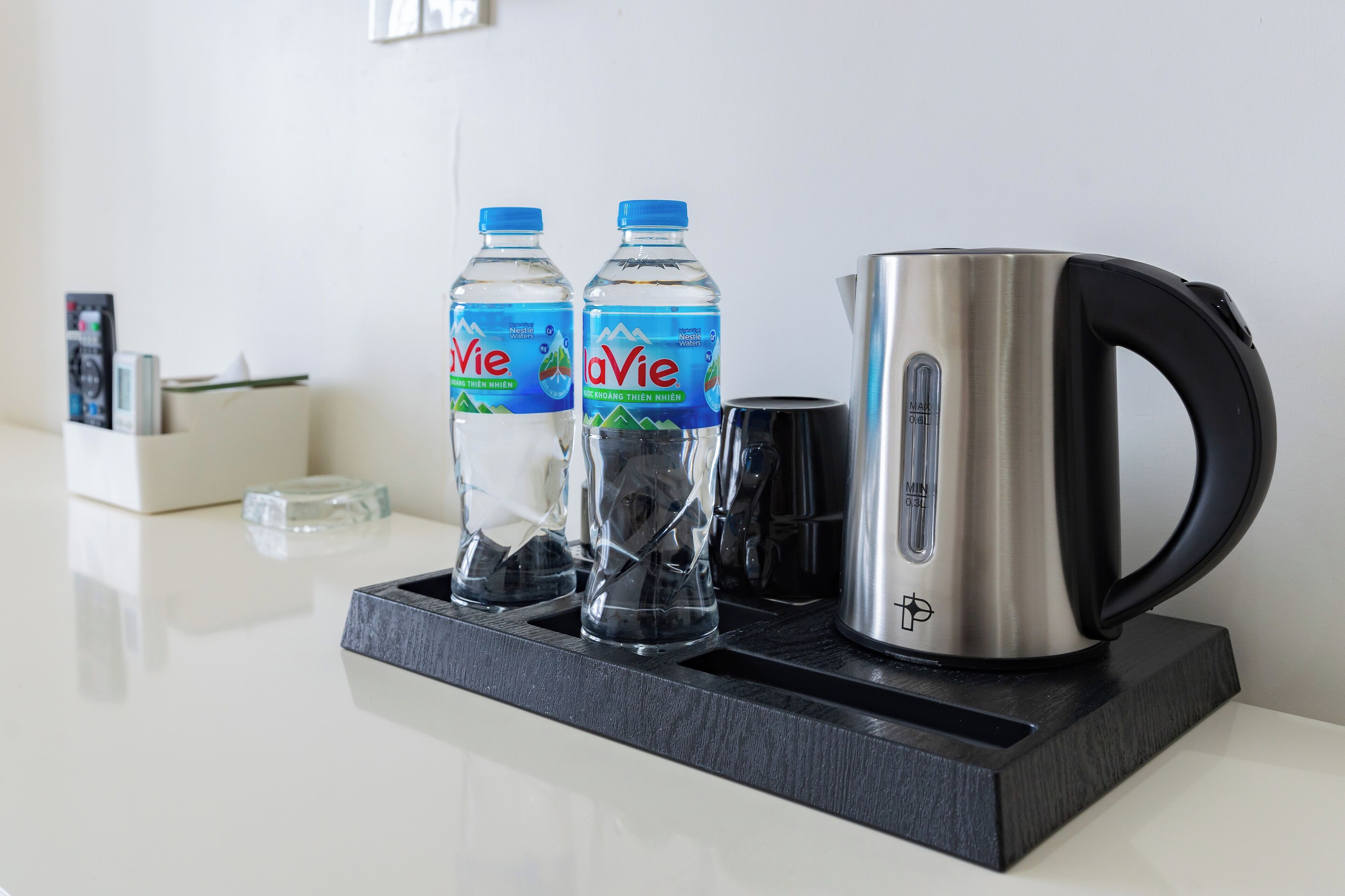 Eine Küchenzeile mit zwei LaVie-Wasserflaschen, einem Edelstahlkocher und einer Glas Karaffe auf einer schwarzen Ablagefläche.
