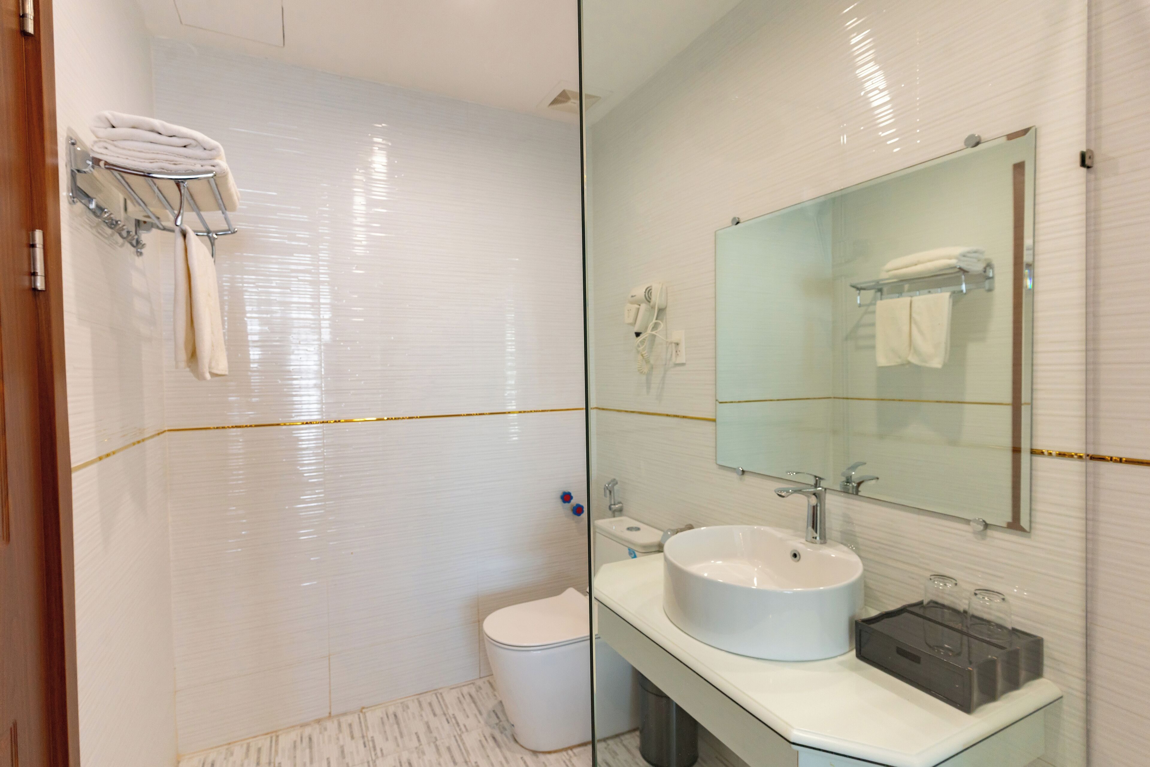 Un baño moderno con cabina de ducha de vidrio, inodoro blanco, lavabo con espejo y toallero con toallas dobladas.