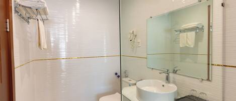 Un baño moderno con cabina de ducha de vidrio, inodoro blanco, lavabo con espejo y toallero con toallas dobladas.