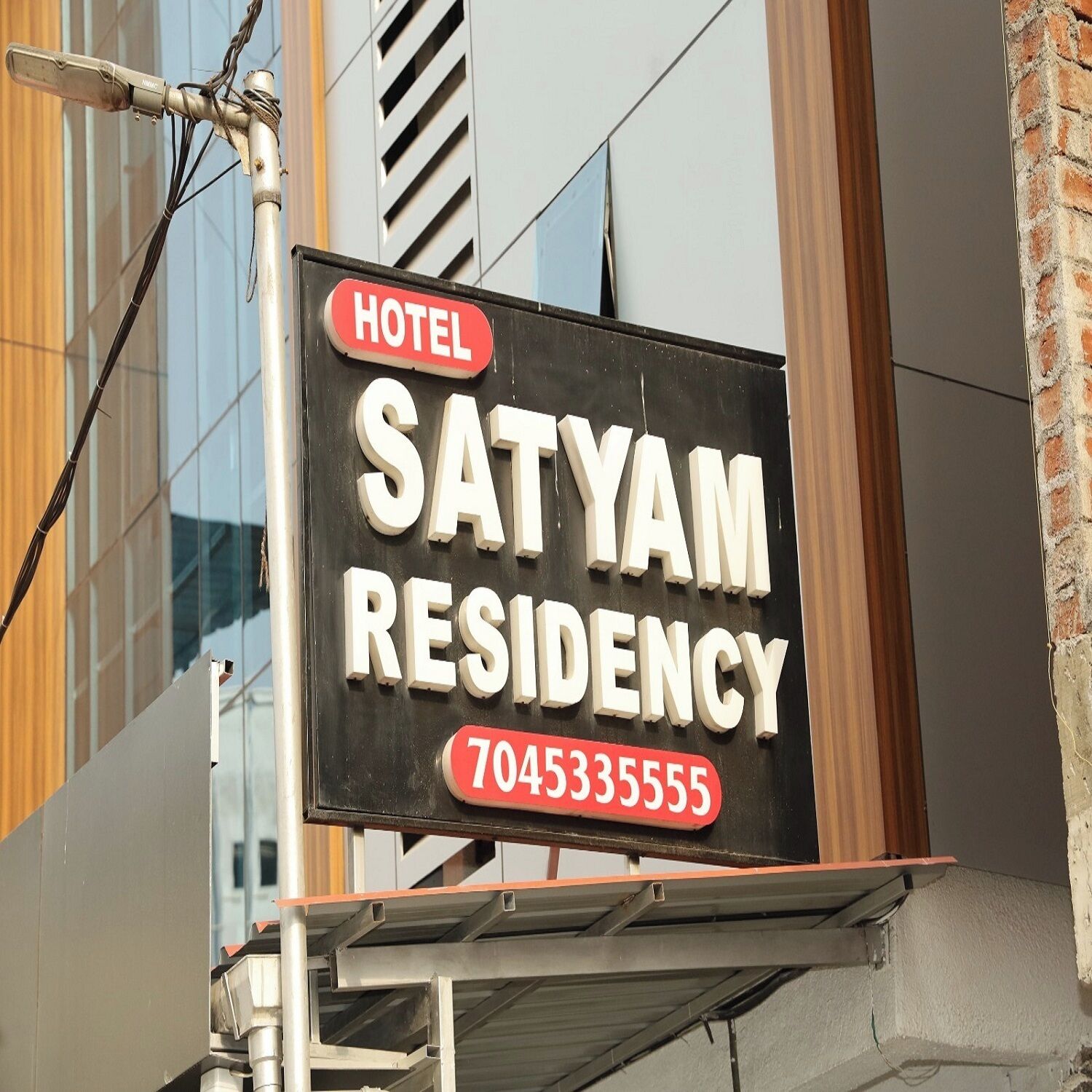 A sign for Satyam Residency, a hotel, with a contact number 7045335555.