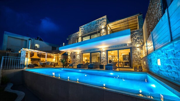 Ein modernes Haus mit Swimmingpool, Sitzgelegenheiten im Freien und Steinmauern.