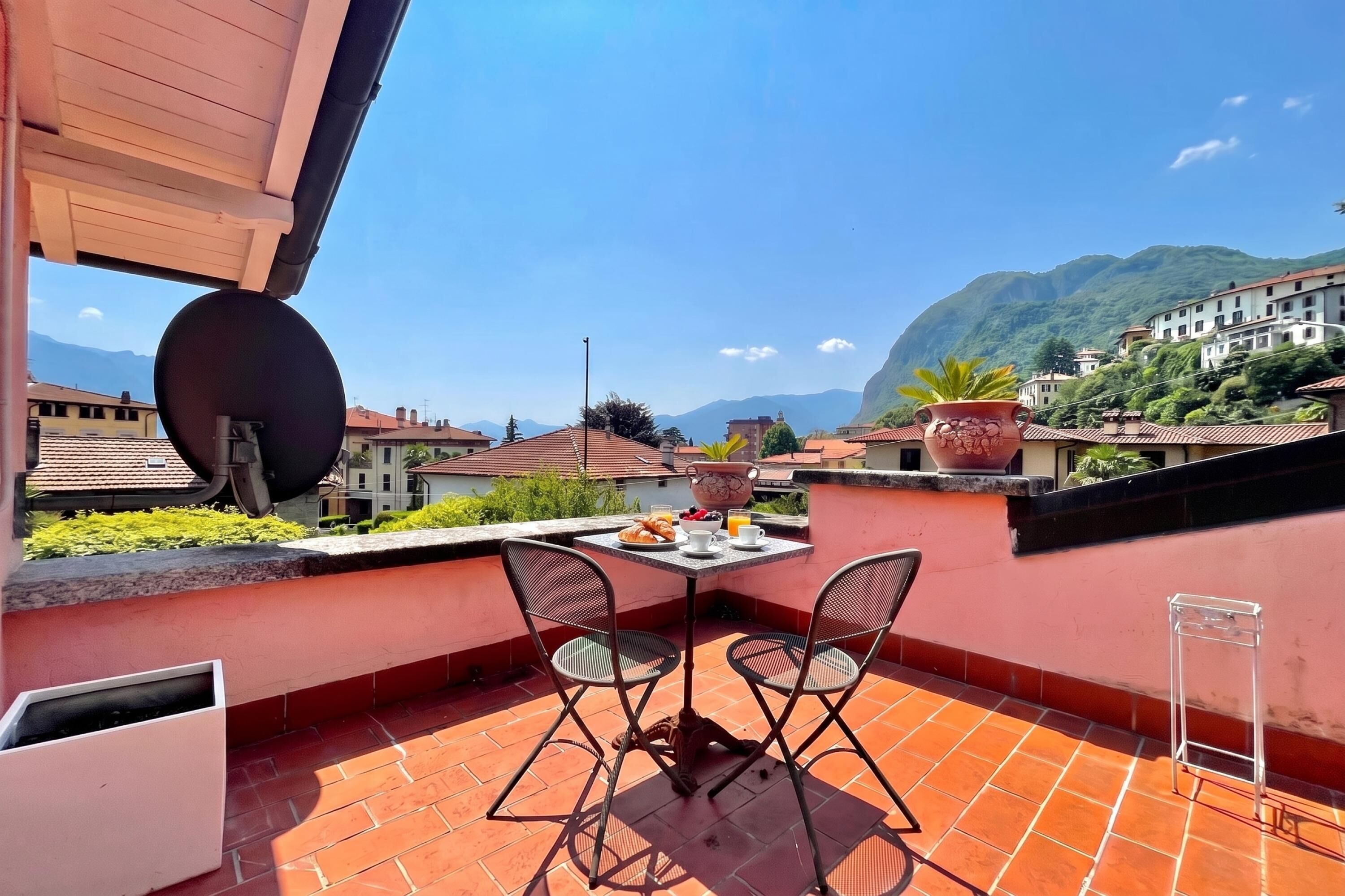 A terrace with a table set for breakfast, two chairs, a potted plant, and a view of a mountain.