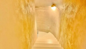 Una escalera blanca en una habitación estrecha y con textura, con una lámpara en la parte superior.