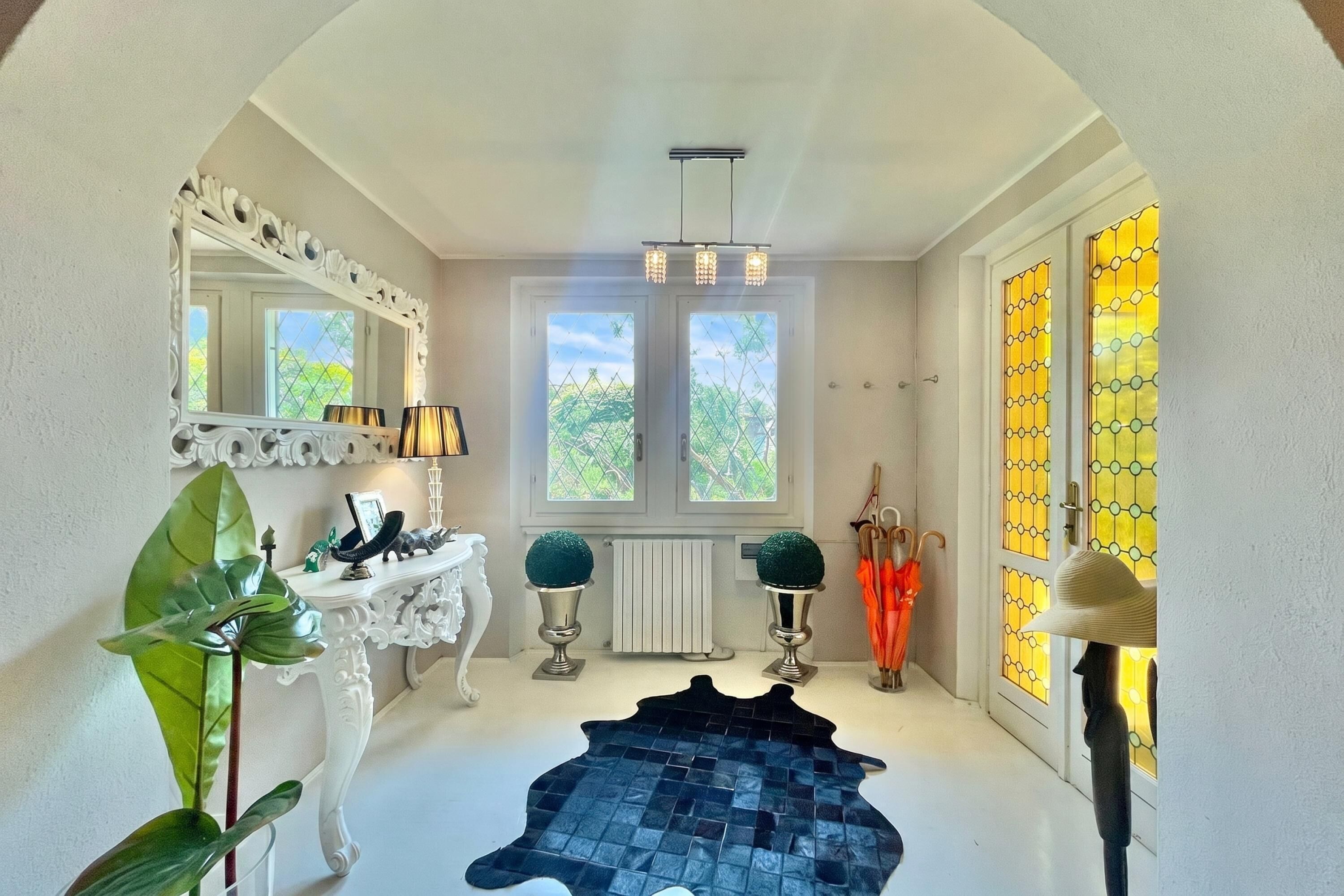 A hallway with a white console table, a large mirror, a black rug, and a window with a view of greenery.