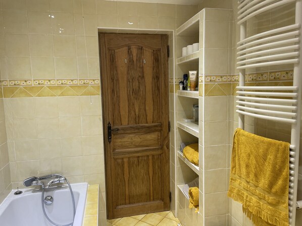A bathroom with a wooden door, a white bathtub with a showerhead, and a towel rack with a yellow towel. - Spacious Provençal villa in an absolutely quiet location. (Roquefort-les-Pins)