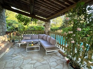 A covered patio with a stone floor, a beige sectional sofa, a coffee table, and a wooden pergola. - Spacious Provencal villa in absolute calm. (Roquefort-les-Pins)
