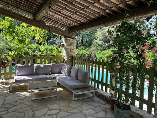 A covered outdoor seating area with a stone floor, a wooden pergola, and a view of a pool. - Spacious Provencal villa in absolute calm. (Roquefort-les-Pins)