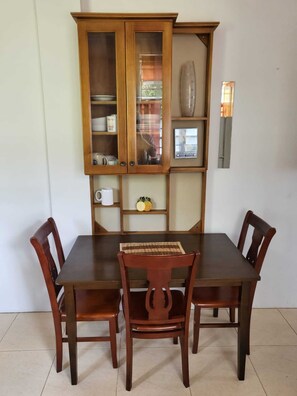 Uma mesa de jantar com quatro cadeiras de madeira e um armário de madeira com portas de vidro.