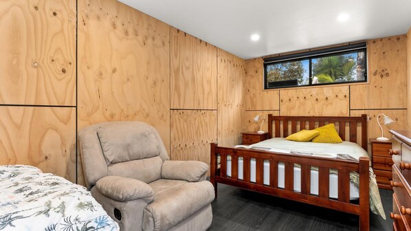 Une chambre avec un mur lambrissé en bois, un lit avec une tête de lit en bois, une chaise et une fenêtre donnant sur des arbres.