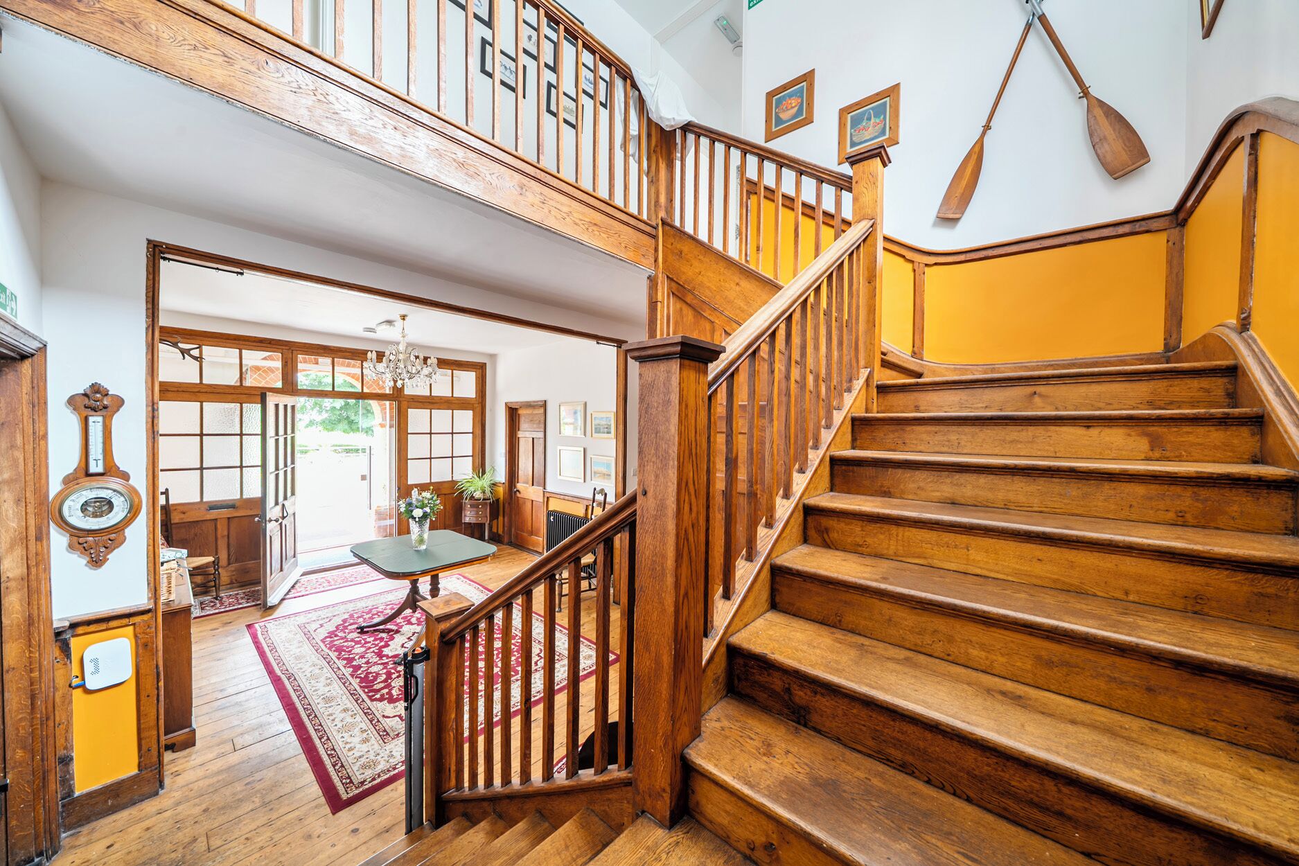 A wooden staircase with a view of a room with a red and white patterned rug, a wooden table with a vase, and a door leading outside.