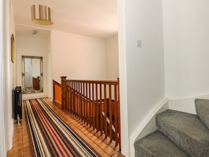 Ein Flur mit einer Holztreppe, einem Streifenmuster-Teppich und einem Spiegel an der Wand.