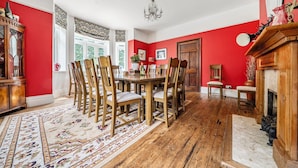 A dining room with a wooden table and chairs, a chandelier, and a fireplace.