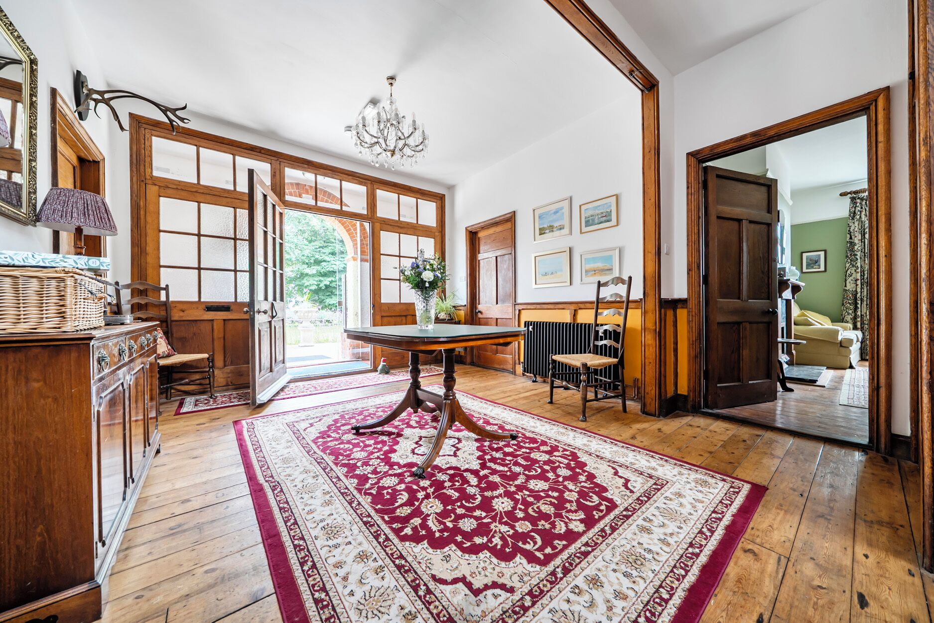 A room with a wooden floor, a dining table with chairs, a chandelier, and a large window.
