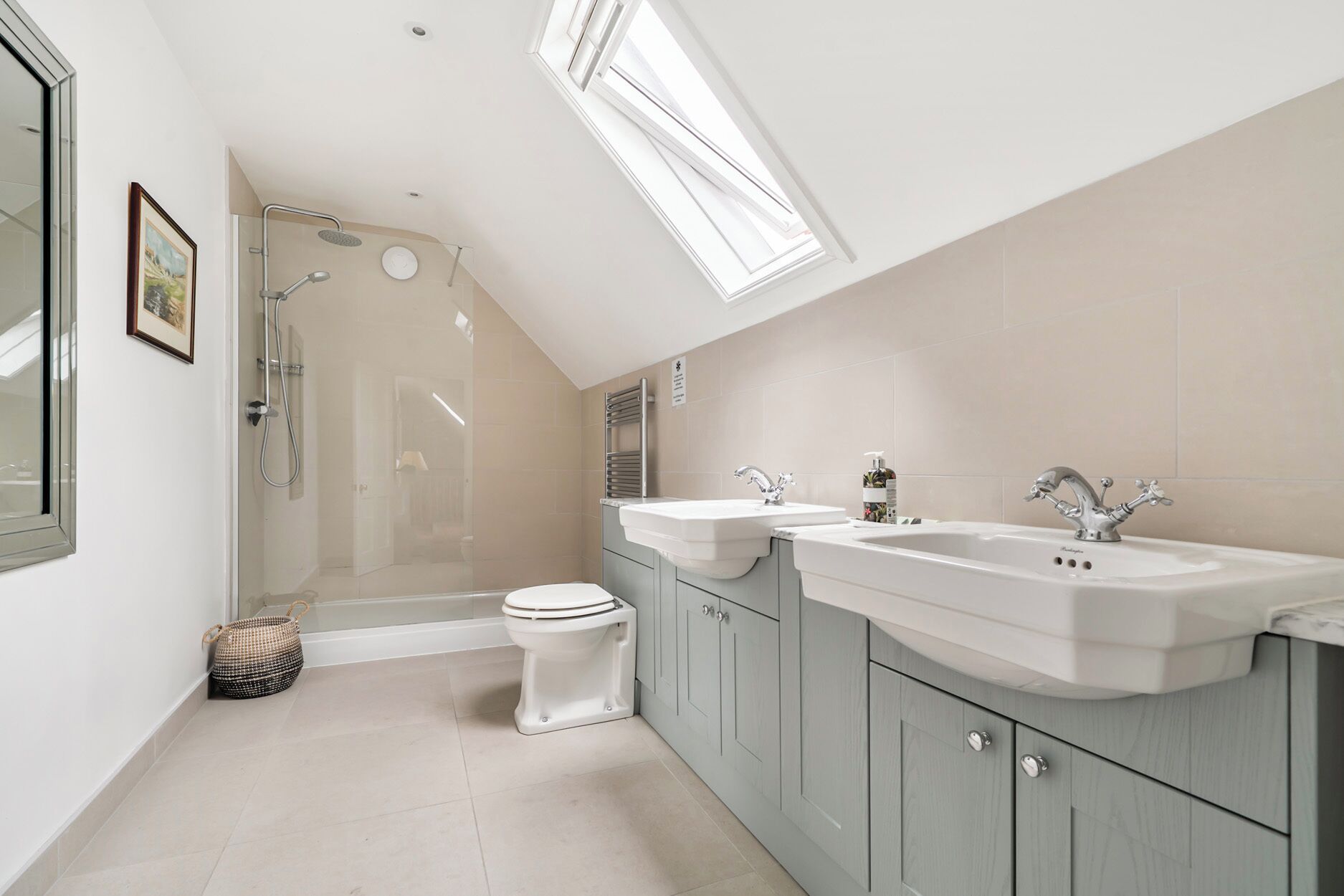 A modern bathroom with a skylight, two sinks, a toilet, and a shower.