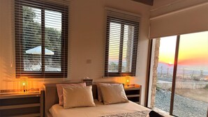 Une chambre avec un grand lit, deux tables de chevet et une vue sur le coucher de soleil par la fenêtre.