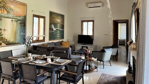 Un vaste espace de vie doté d’un haut plafond, d’un téléviseur à écran plat, d’une table à manger pour quatre personnes et de deux canapés.