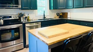 A modern kitchen with dark teal cabinets, stainless steel appliances, and a wooden island with a cutting board. - Cozy and Charming Cottage in Kerhonkson (Kerhonkson)