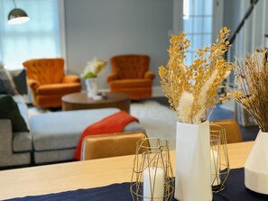 Een moderne woonkamer met een bank, twee fauteuils, een salontafel en decoratieve vazen met gedroogde planten.
