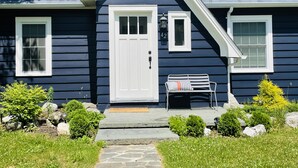 A dark blue house with a white door, two windows, a bench, and a small garden with rocks and plants. - Cozy and Charming Cottage in Kerhonkson (Kerhonkson)