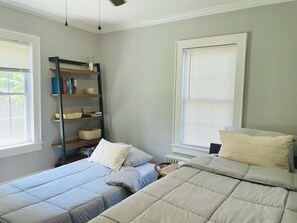 Een slaapkamer met twee bedden, een boekenkast en een raam met zonwering.
