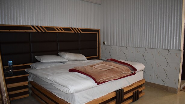 A bed with a wooden frame and a headboard with a geometric design. - Clifton Hotel (Balakot)