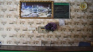 A hotel reception area with a framed picture of a mosque, a clock, and a green sign reading "CLIFTON HOTEL". - Clifton Hotel (Balakot)