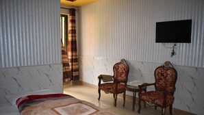 A hotel room with a bed, two armchairs, a small table, and a TV mounted on the wall. - Clifton Hotel (Balakot)