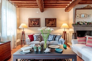 Uma sala de estar com sofá, mesa de centro com objetos decorativos, duas luminárias fixadas na parede e uma lareira com parapeito.