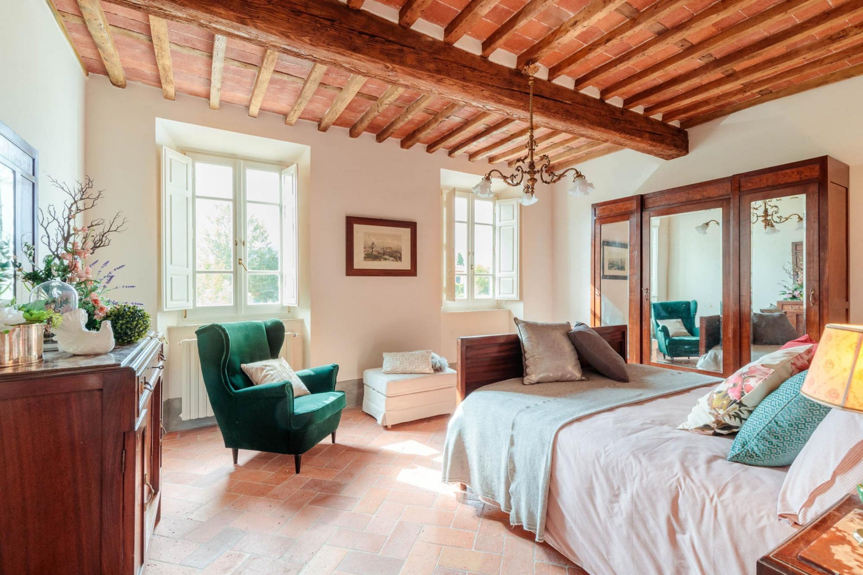 Una camera da letto con un letto grande, una poltrona verde, un comò in legno e uno specchio.
