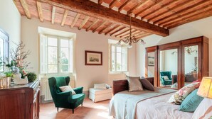 Quarto com uma cama grande, uma poltrona verde, uma cômoda de madeira e um espelho.